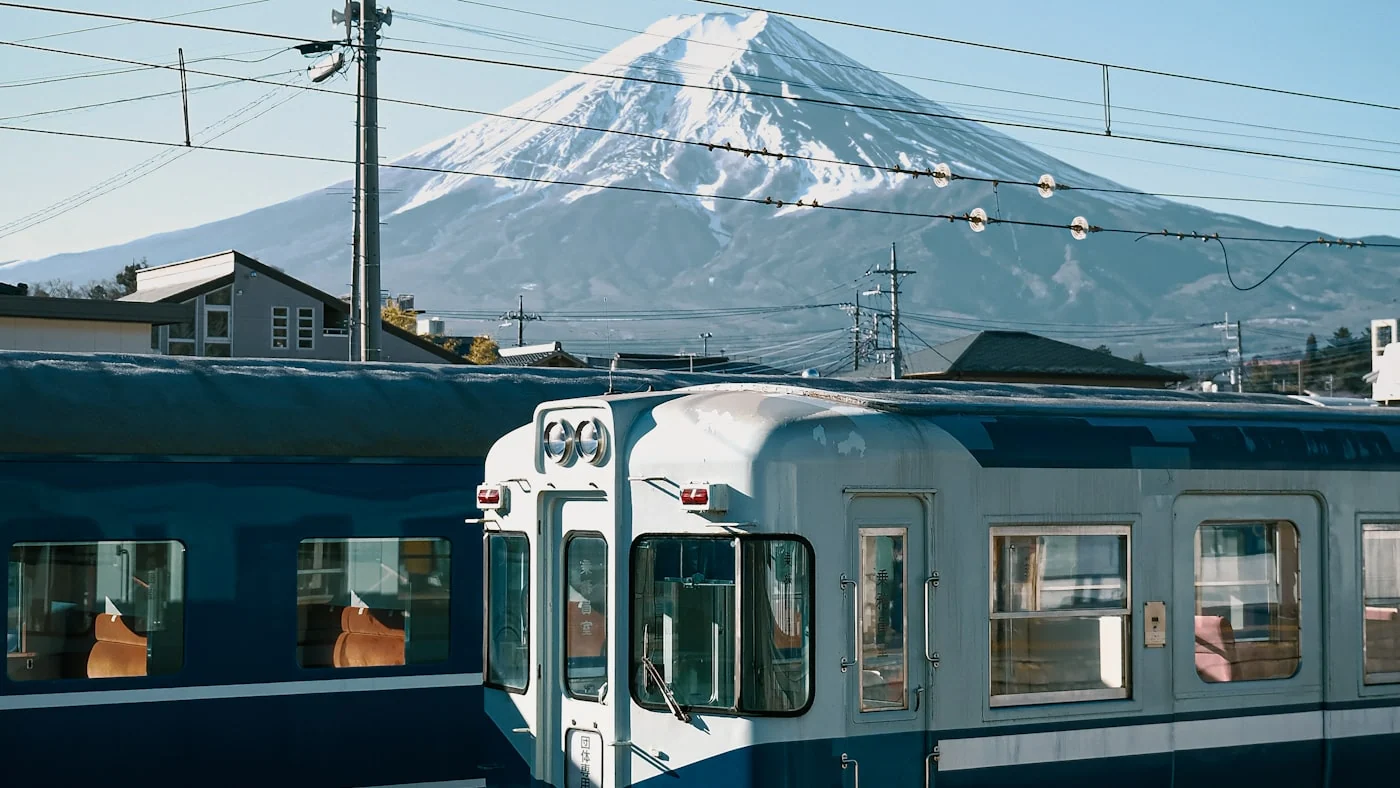 Tren azul y blanco pasando frente al monte Fuji nevado.