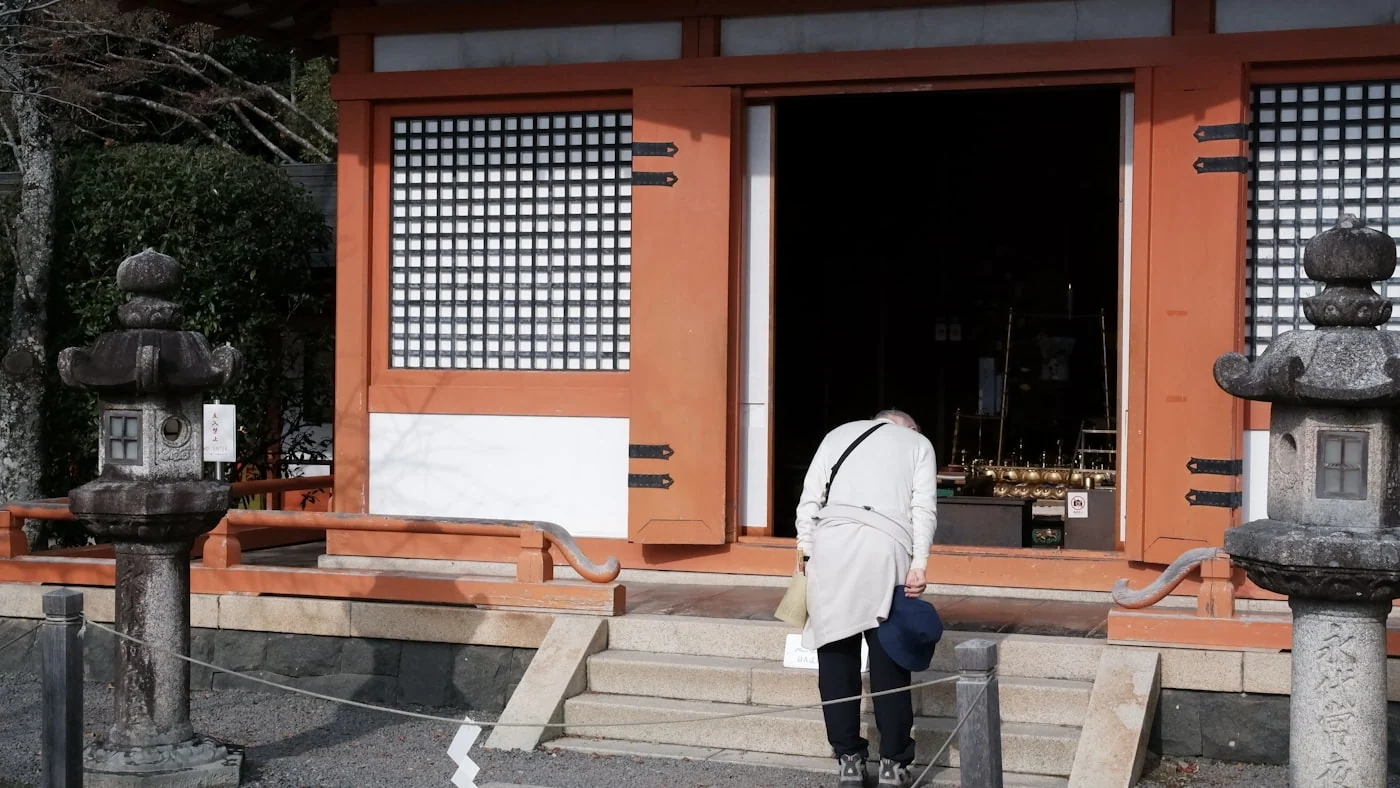 Persona inclinándose frente a la entrada de un templo japonés.